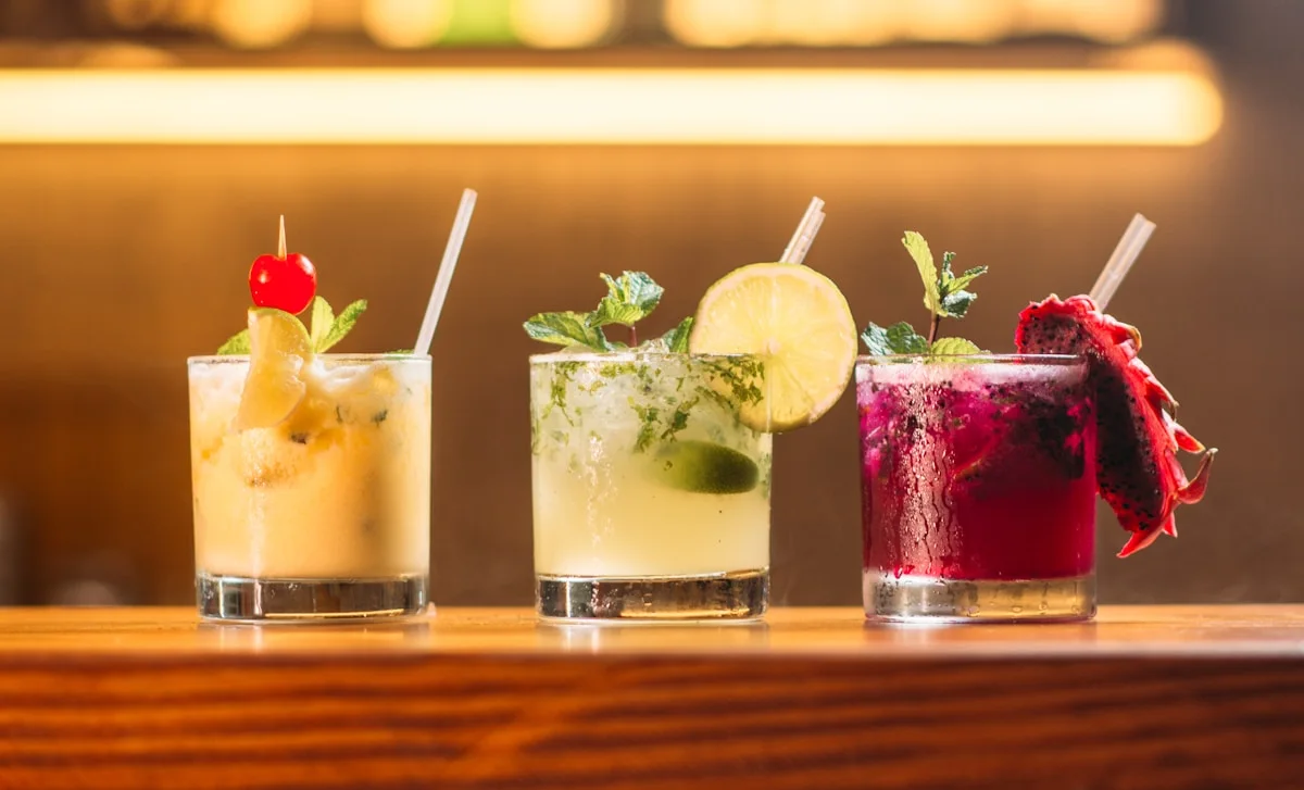 Three colorful botanical drinks on a warmly lit bar